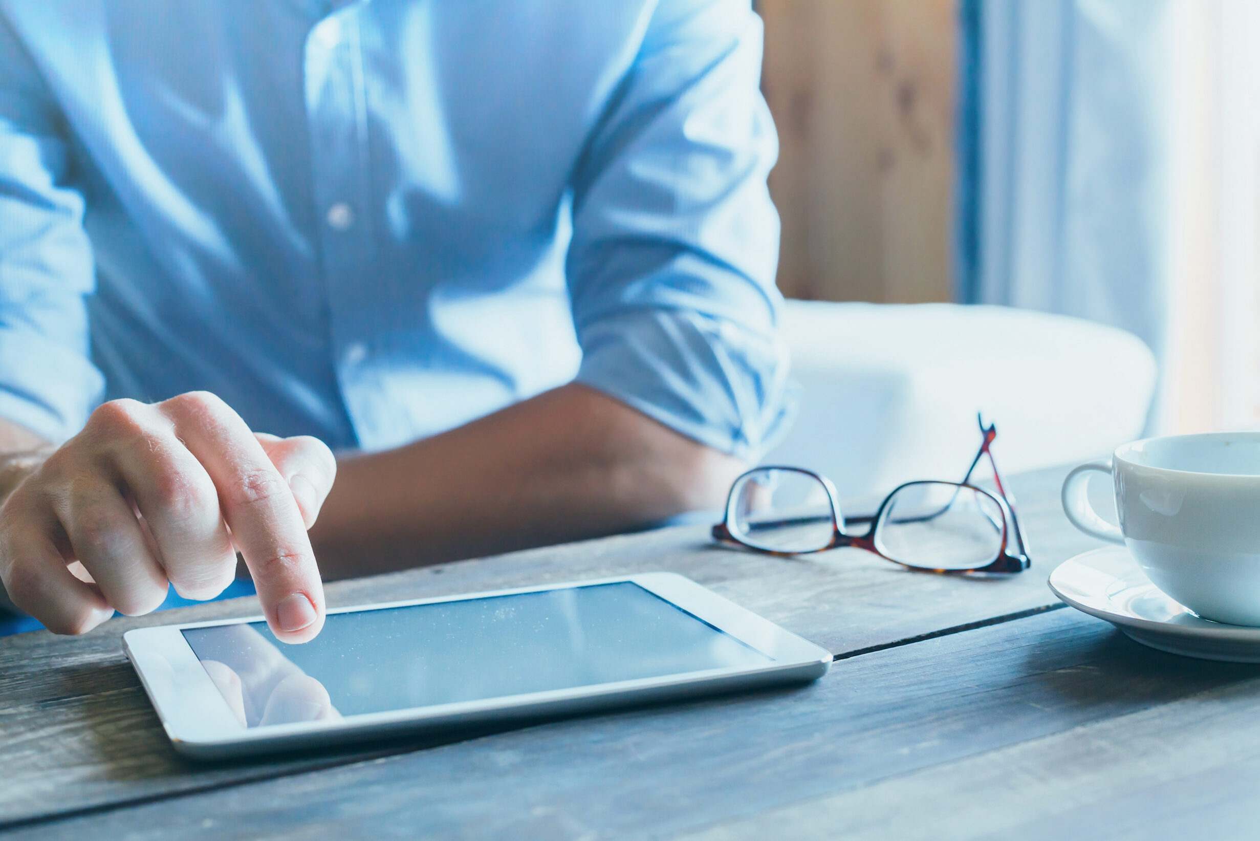 A man points at a tablet with his glasses sitting on the desk next to him.